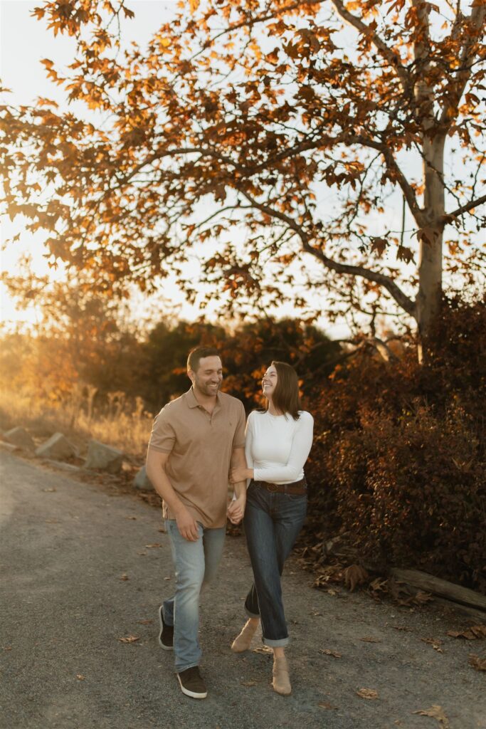 Couple walking hand-in-hand along a rustic path surrounded by vibrant autumn trees.