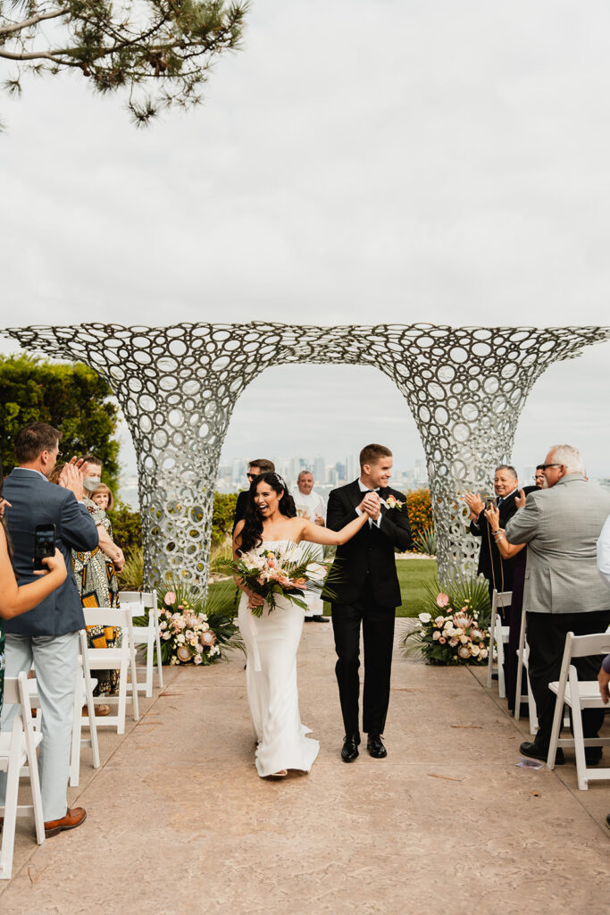 Bride and groom celebrate as they walk down the aisle after an outdoor ceremony with modern architectural decor and scenic views.