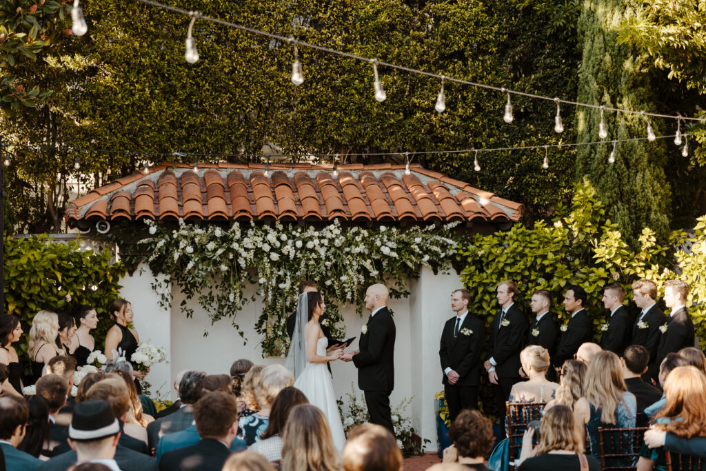 Bride and groom exchange vows in an intimate garden wedding ceremony adorned with lush greenery and white floral arrangements.