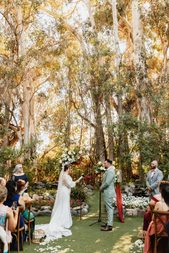 Bride and groom exchange vows during an intimate outdoor ceremony surrounded by towering eucalyptus trees and floral decor.