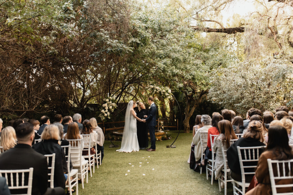 Bride and groom exchange vows under a canopy of lush trees in an intimate outdoor wedding ceremony.