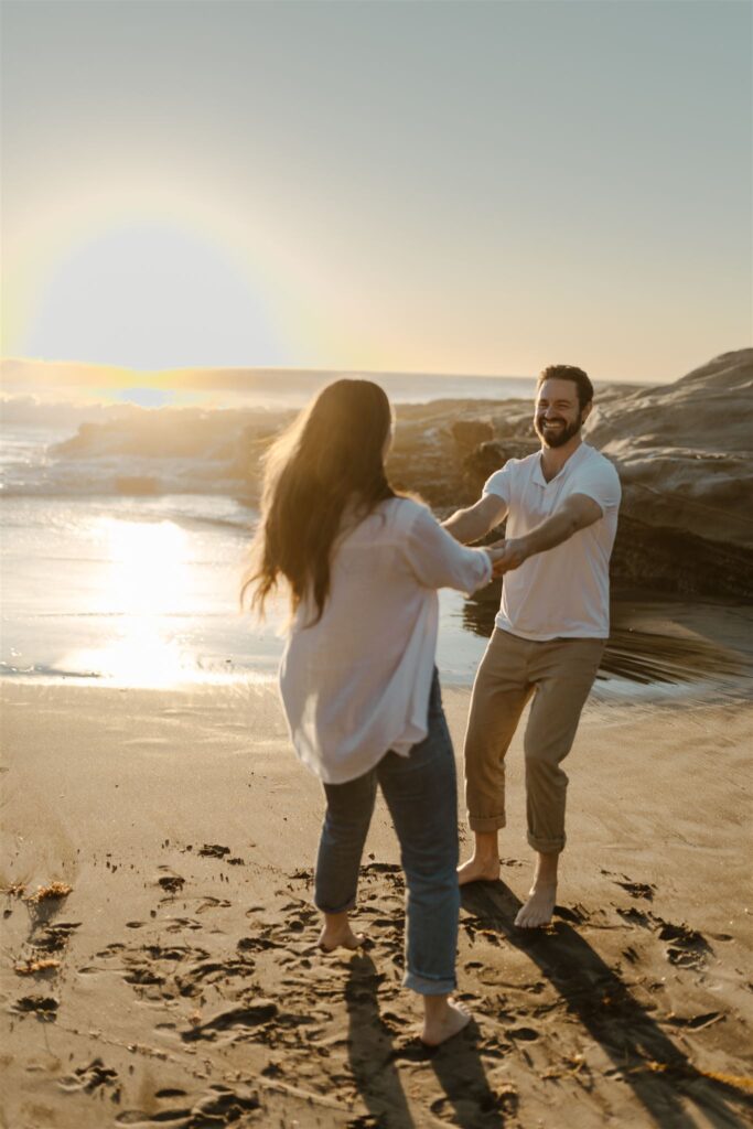 Couple laughing and spinning on the beach during a fun sunset engagement session.