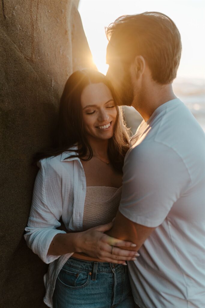 Romantic couple sharing an intimate embrace at sunset by a rocky beach.