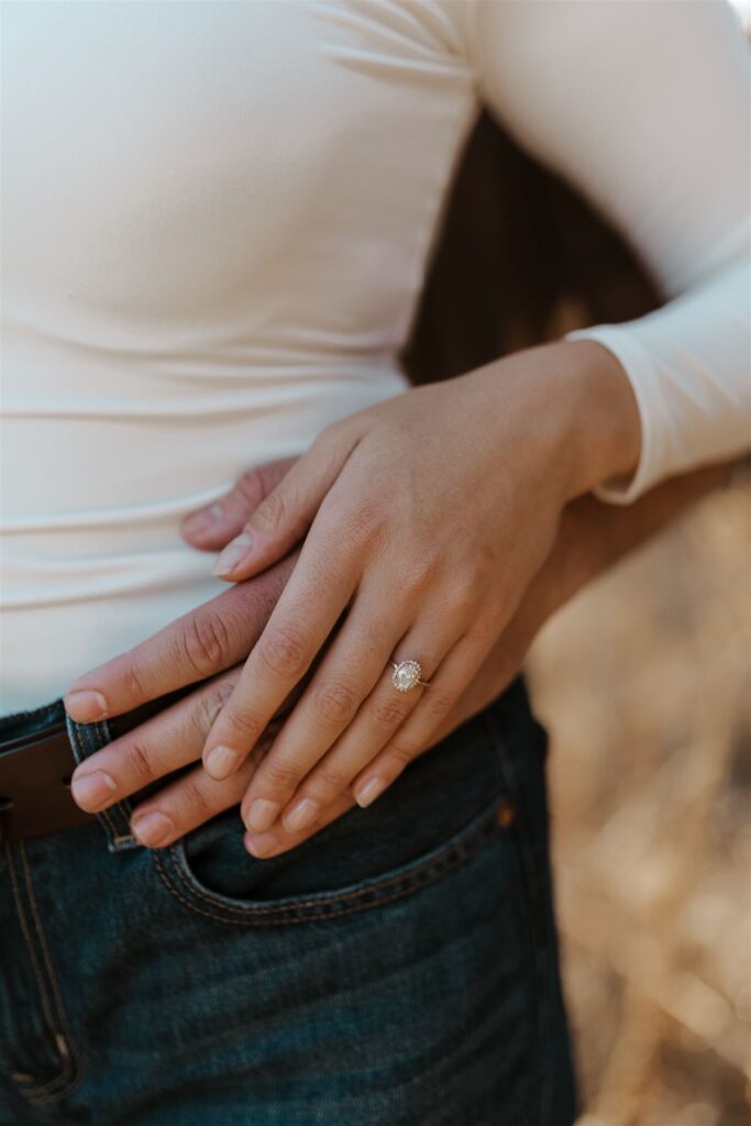 Close-up of an engagement ring on a woman’s hand resting on her fiancé’s hand.