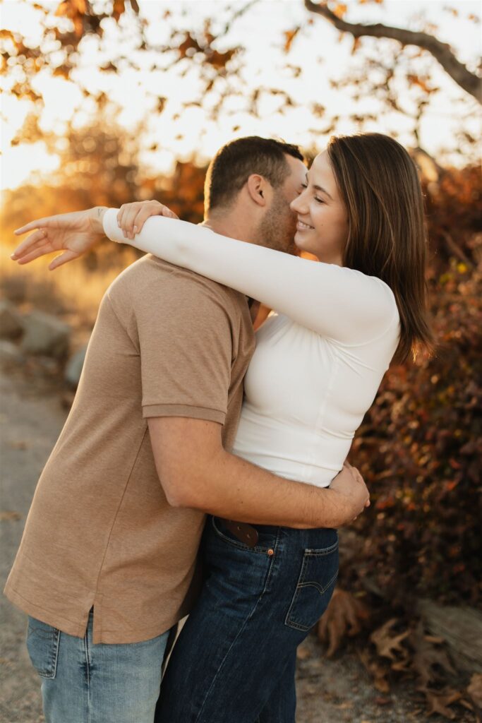 Couple embracing during a golden-hour engagement session surrounded by fall foliage.
