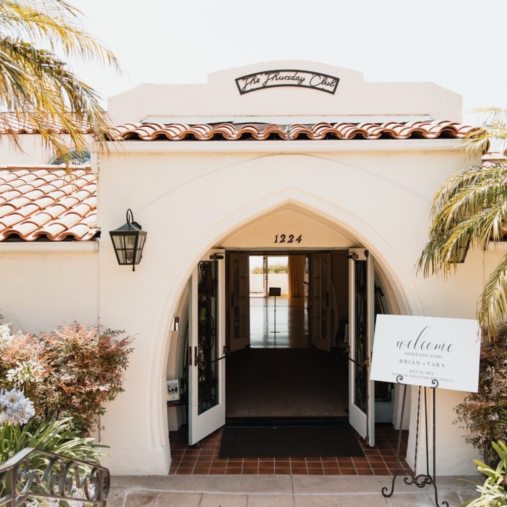 Elegant Spanish-style wedding venue entrance with an arched doorway and a welcome sign for guests.